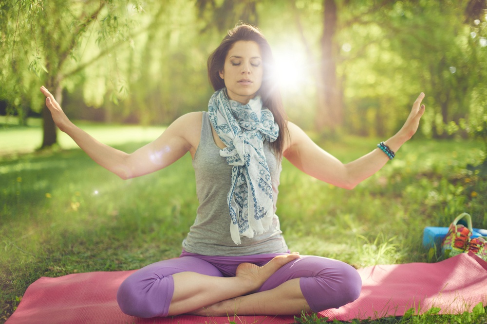 Serene and peaceful woman practicing mindful awareness by meditating in nature with sun flare.